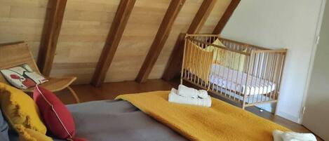 Una habitación acogedora con cama, almohadas, una cuna y una lámpara colgante.