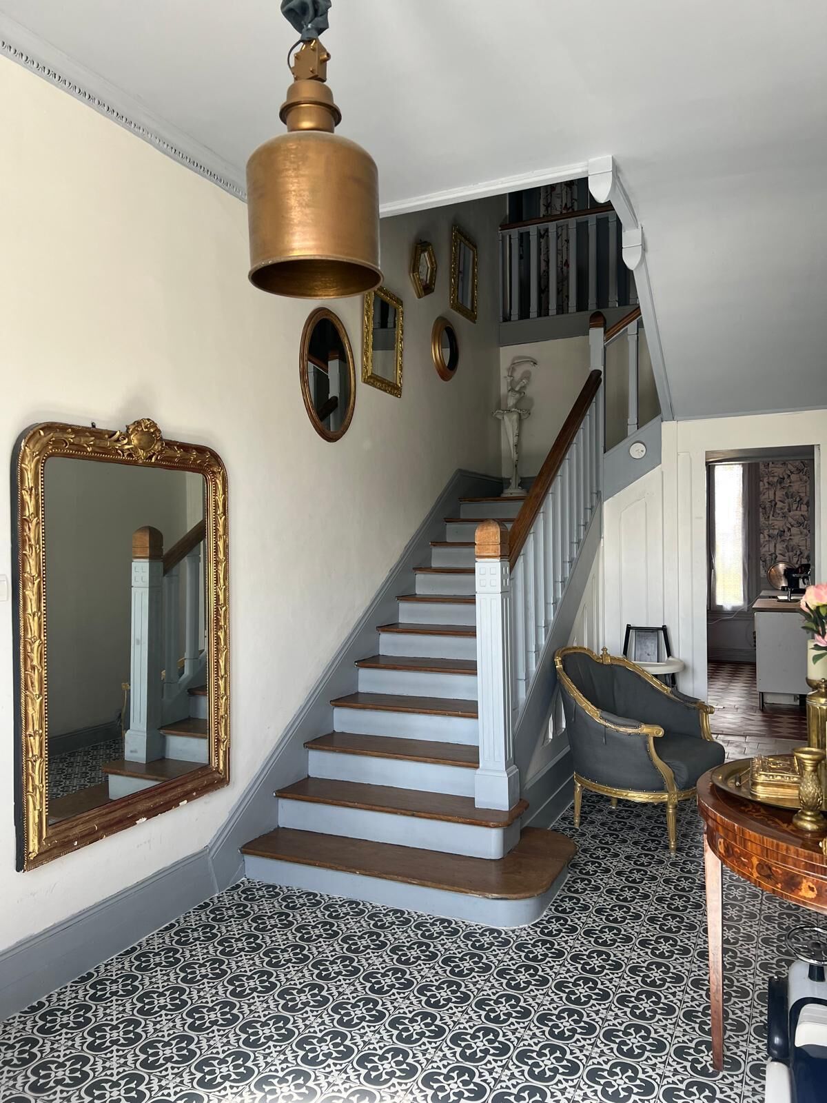 Un escalier avec des marches en bois et des balustrades blanches, menant à un palier agrémenté d’un grand miroir et de tableaux encadrés.
