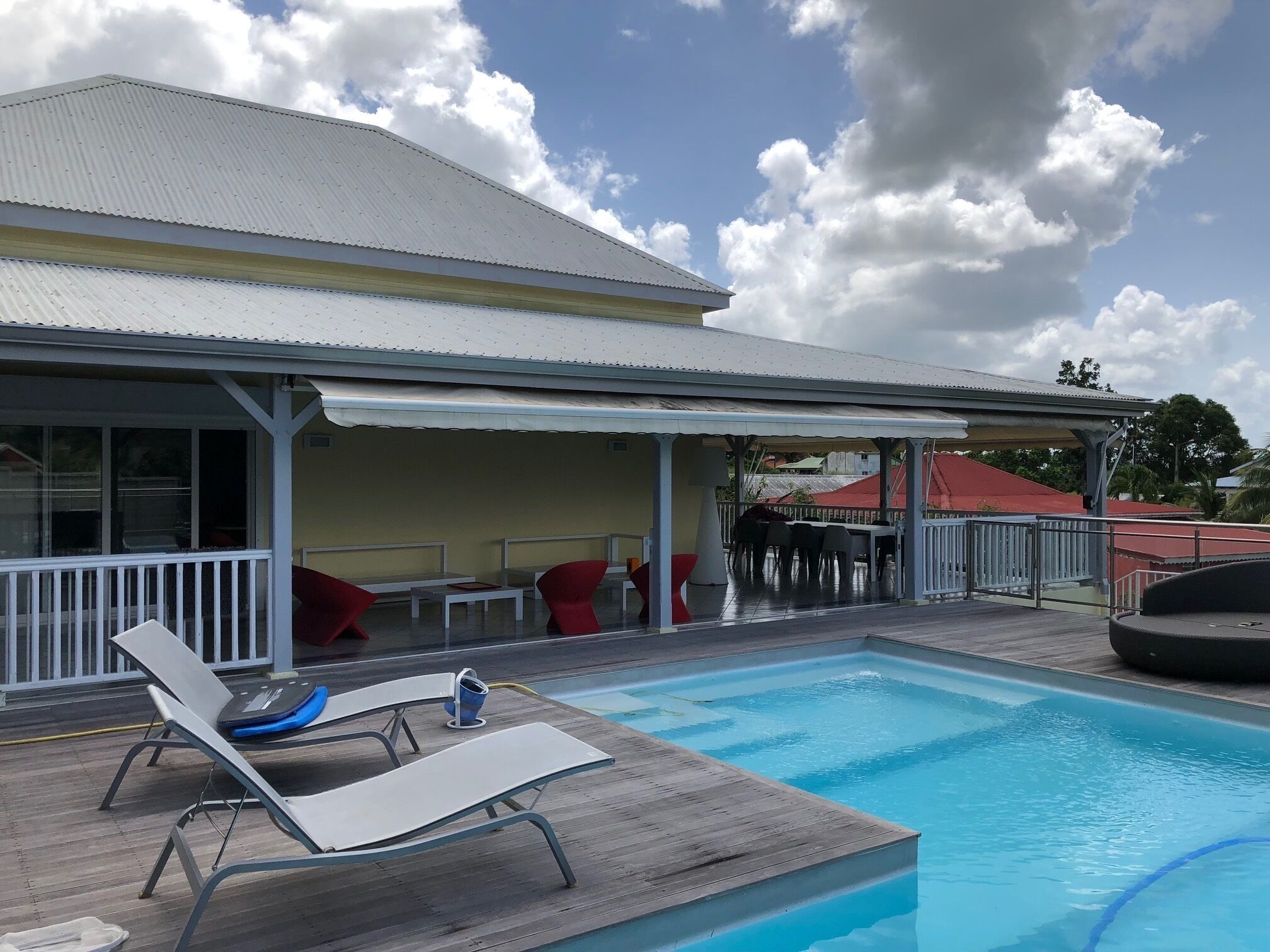 Un área de piscina con sillones reclinables, un porche cubierto y un edificio con techo de metal corrugado.