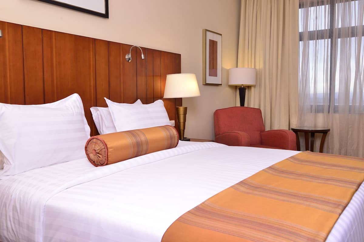 A hotel room with a large bed, two bedside lamps, a red armchair, and a small table.