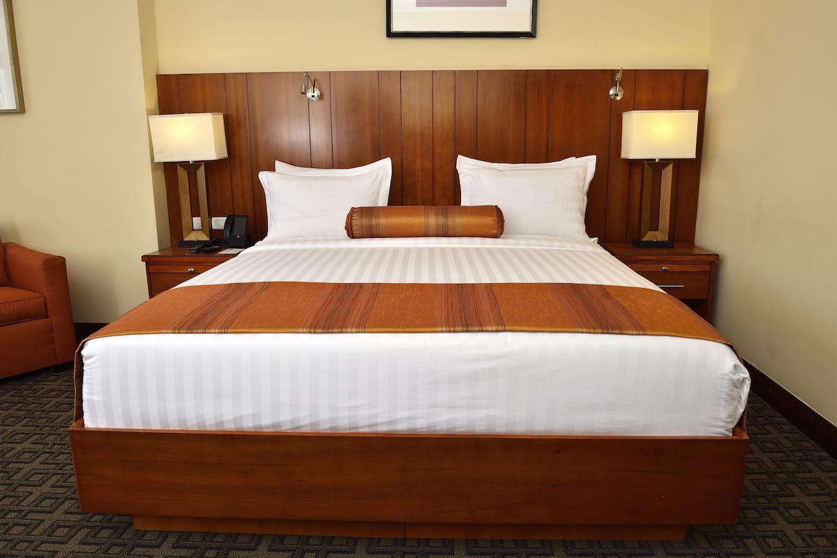 A large bed with a wooden headboard, two bedside lamps, and a single decorative pillow.