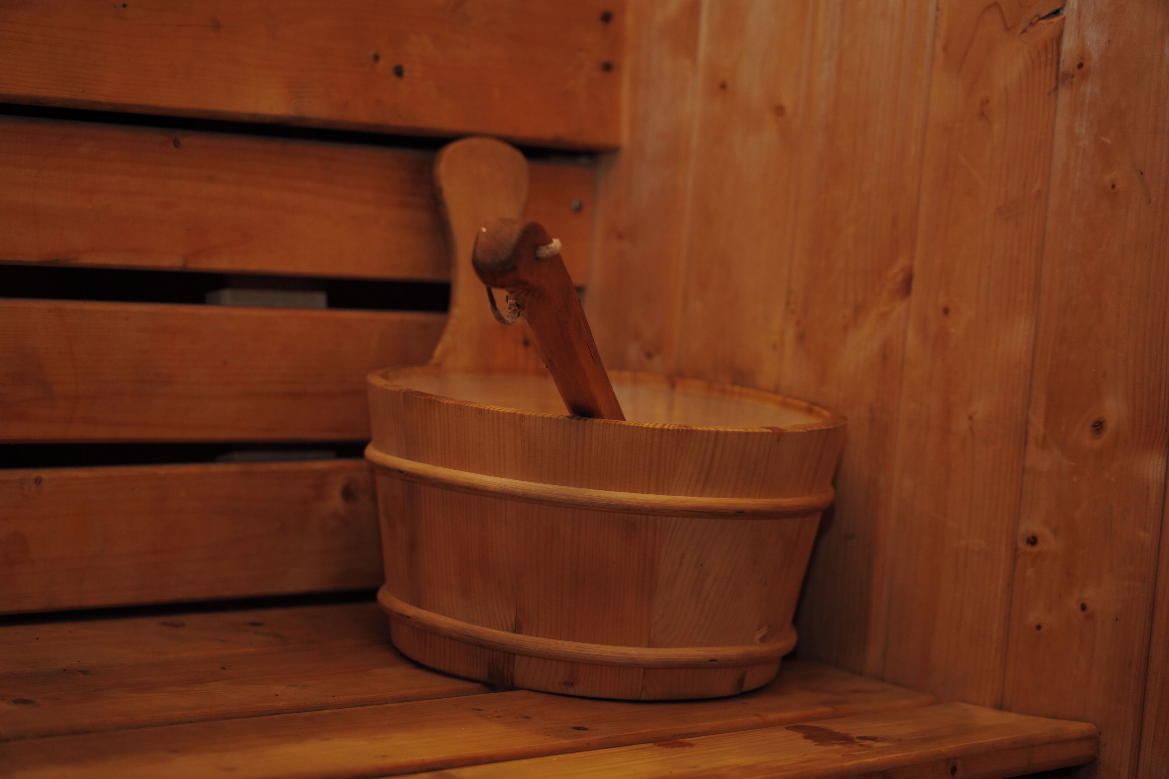A wooden bucket with a handle, placed on a wooden bench in a room with wooden walls.