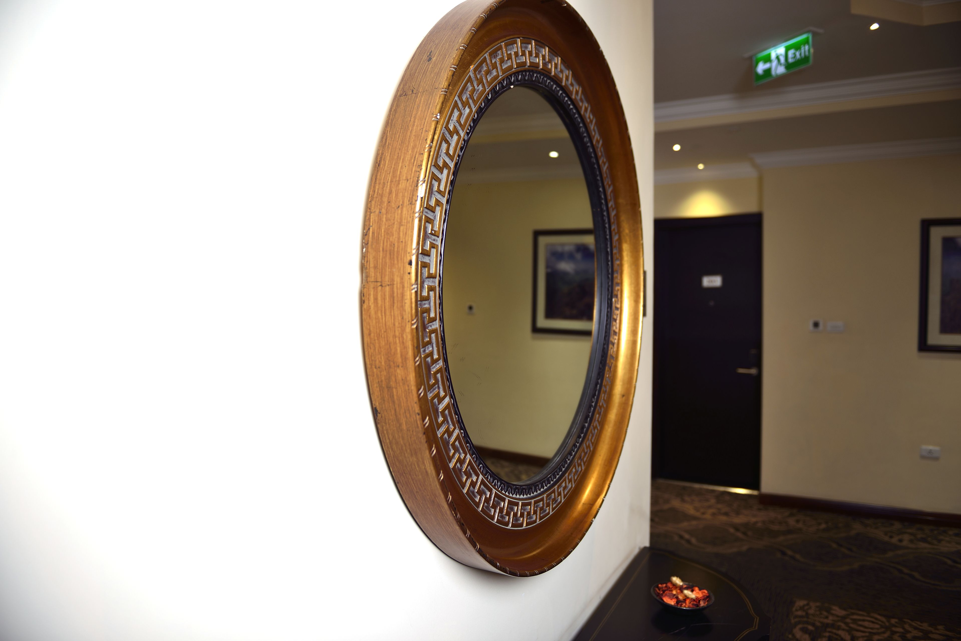 Een ronde spiegel met decoratieve lijst bevestigd aan een wand in een hotelkamer.