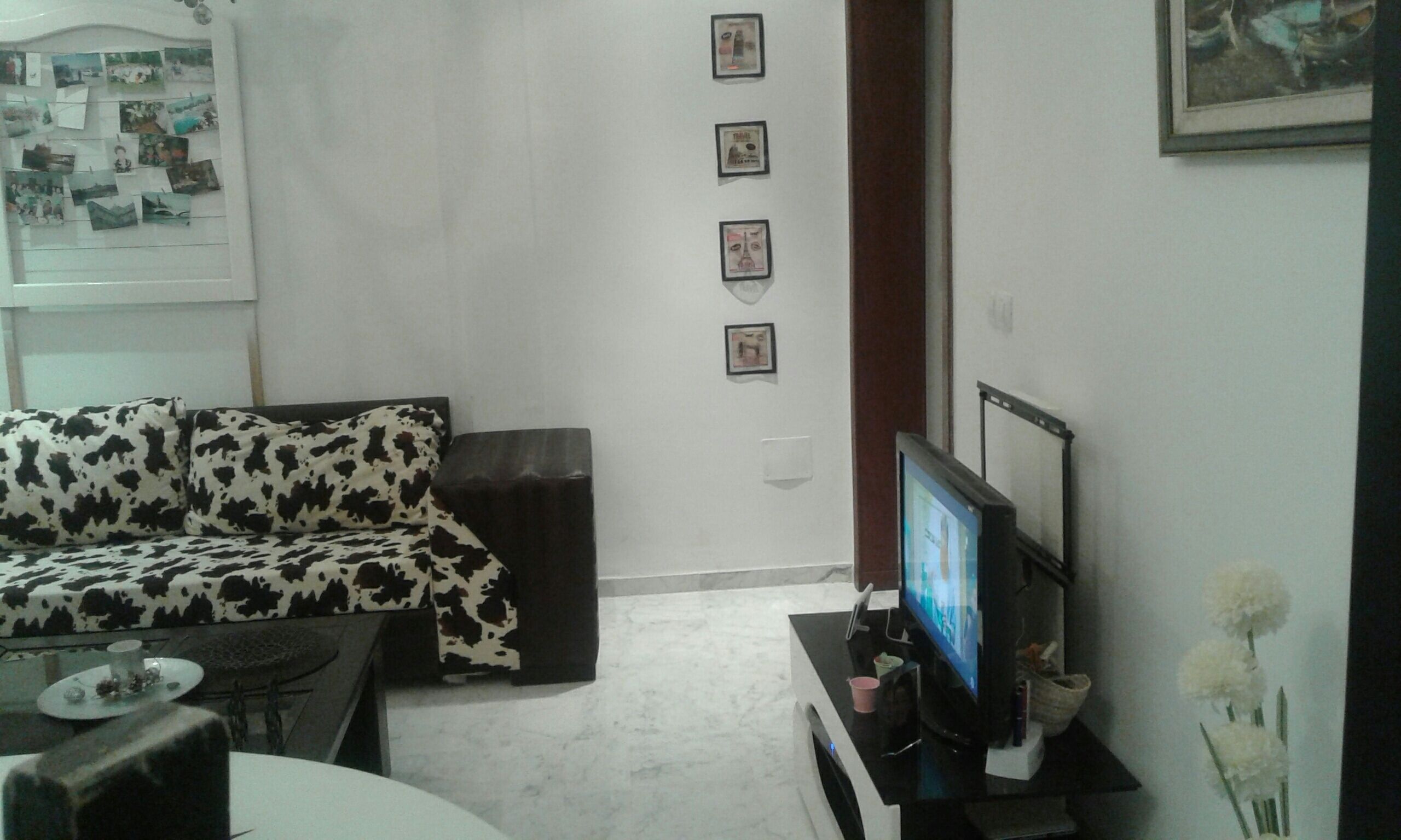 A living room with a sofa, a TV on a stand, and a wall with framed pictures.