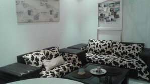 Un salón moderno con un sofá de estampado vaca en blanco y negro, una mesa de centro de cristal y un collage de fotos en la pared.