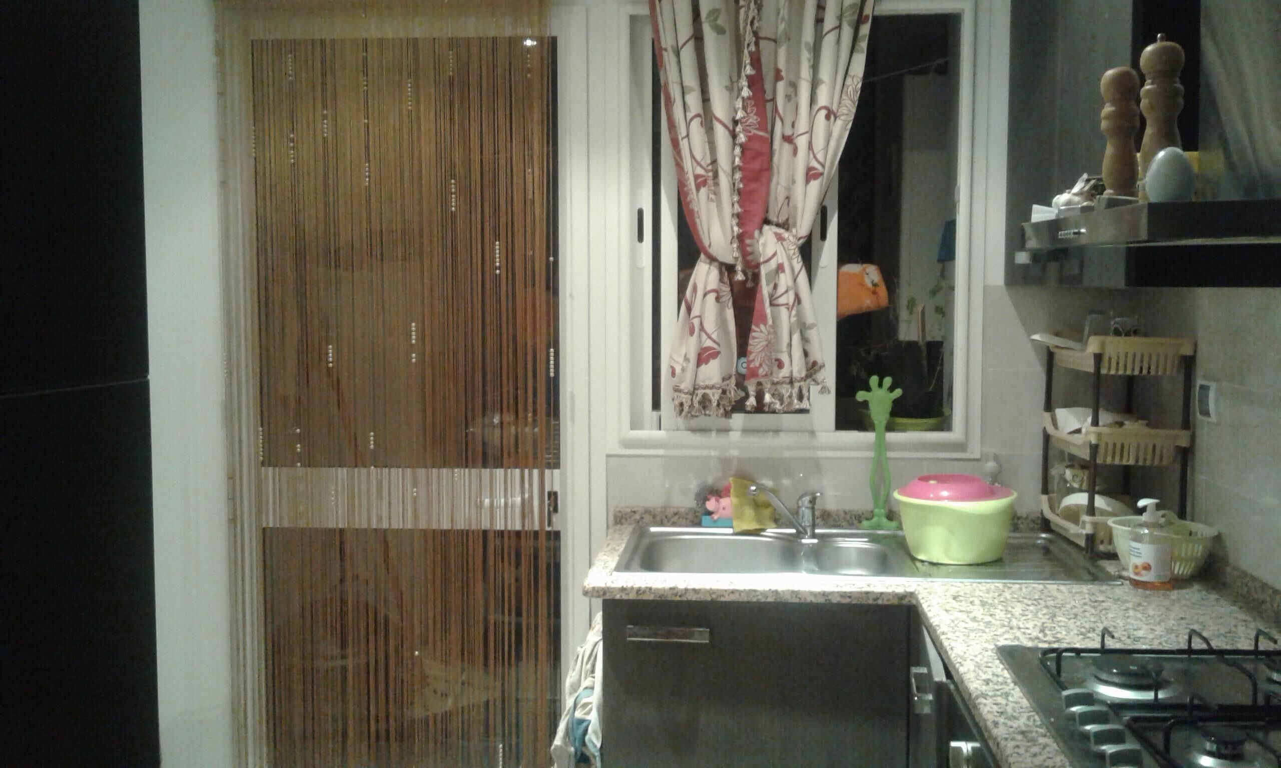 A kitchen with a sink, a gas stove, and a window with curtains.