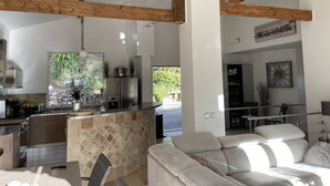 Une cuisine moderne dotée d’un grand îlot central, de poutres en bois et offrant une vue sur l’extérieur.
