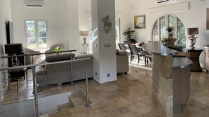 Un vaste espace de vie doté d’un haut plafond, un coin repas avec une table ronde, et une vue sur l’extérieur grâce à de grandes fenêtres.