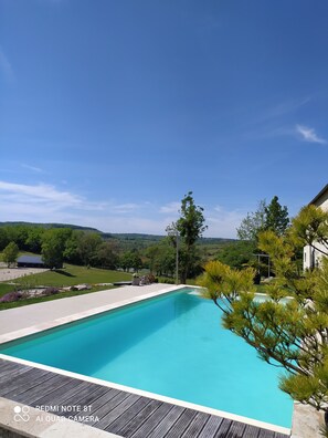 Piscina com deck de madeira, cercada por vegetação e vista para uma paisagem montanhosa.