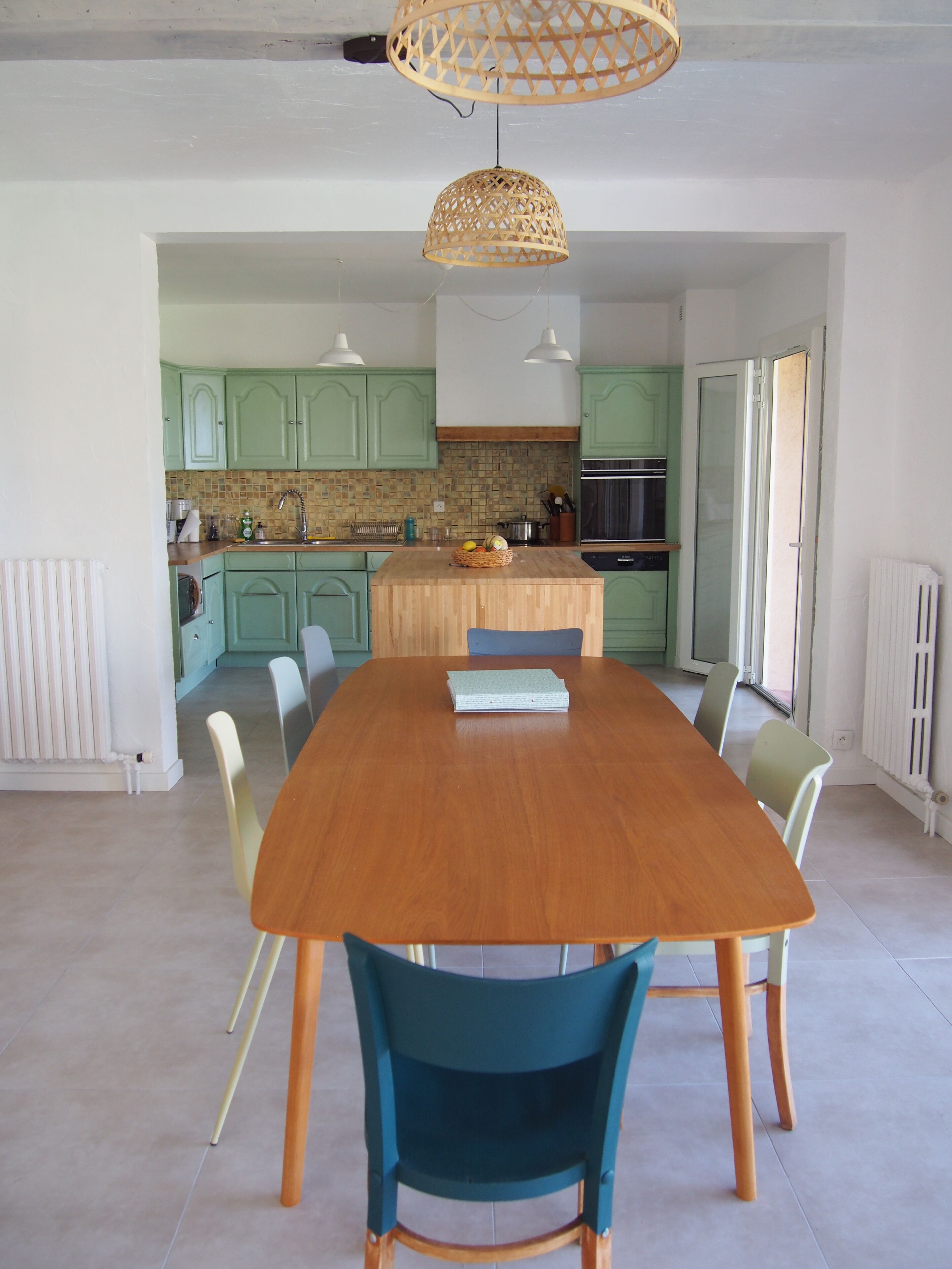 A modern kitchen with green cabinets, a wooden island, and a dining table with chairs.