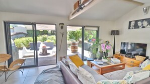 A modern living room with a sofa, a coffee table, and a TV. There is a sliding glass door leading to an outdoor patio with a table and chairs.