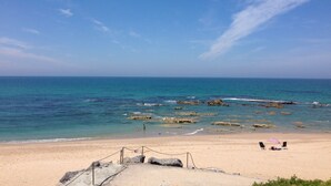A beach with clear skies, calm waters, and rocky outcrops.