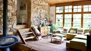 A cozy room with a stone wall, a wooden ceiling, a sofa, a table, and a fireplace.