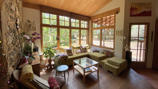 A spacious living room with a high ceiling, large windows, a stone wall, and a cozy seating area.