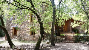 A rustic stone building with a wooden porch, surrounded by trees and a gravel path.