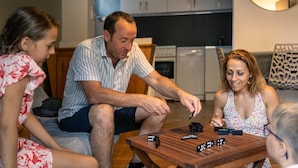 Une famille est réunie autour d’une table en bois dans une cuisine moderne, jouant à un jeu de société. La cuisine est dotée de meubles blancs et d’un plan de travail noir.