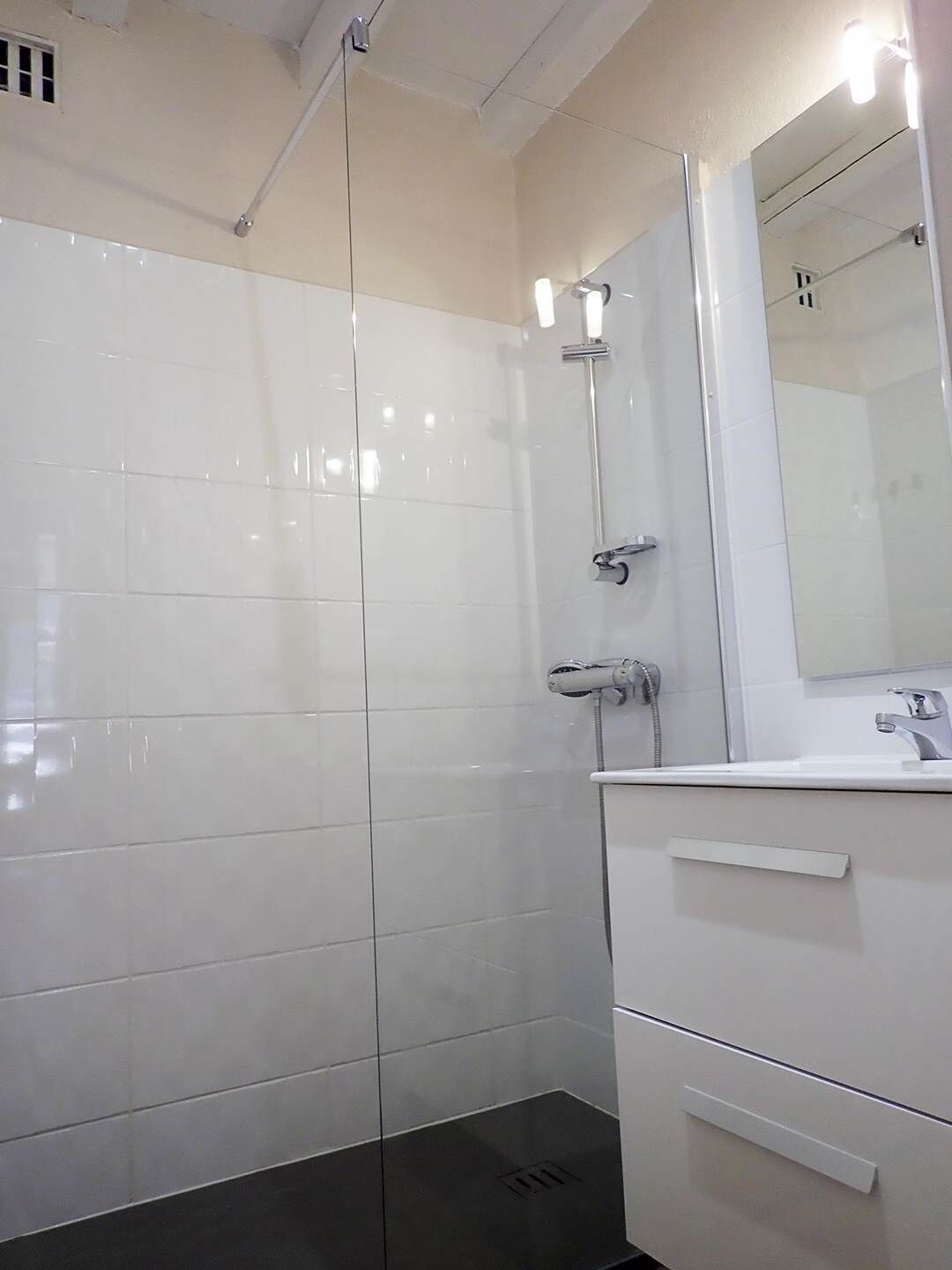 Une salle de bain moderne avec des carreaux blancs, une douche en verre, un lavabo avec un miroir et un porte-serviettes.