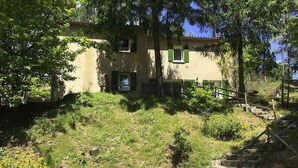 Un bâtiment doté d’un escalier en pierre menant à une porte, le tout entouré de verdure et d’arbres.