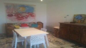 Uma área de refeições com uma mesa e cadeiras brancas, um armário de madeira e um quadro colorido na parede.