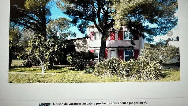 Uma casa de férias com fachada vermelha e branca, cercada por vegetação e árvores.