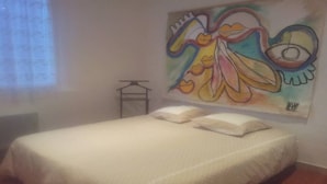 Quarto com cama, almofadas, janela e parede com pintura colorida.