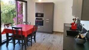 Una cocina moderna con una mesa y sillas rojas, horno empotrado y vistas a un jardín con flores moradas.