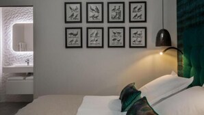 A bedroom with a bed, pillows, a wall-mounted lamp, and framed bird illustrations.