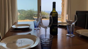 A table set for dining with a bottle of wine, glasses, and plates, overlooking a scenic landscape. - Superb architect villa (TERTENIA DI MARINA)