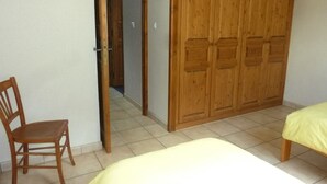 Une chambre avec une armoire en bois, une chaise en bois et un lit recouvert d’une couverture jaune.