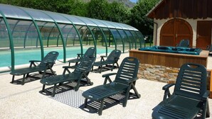 Un espace piscine doté de chaises longues et d’une structure fermée par des parois vitrées.