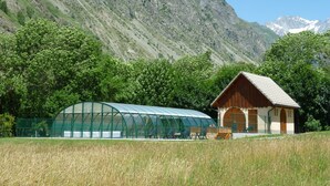 Un chalet de montagne doté d’une serre et d’une cabane en bois, entouré d’une végétation luxuriante et de montagnes.