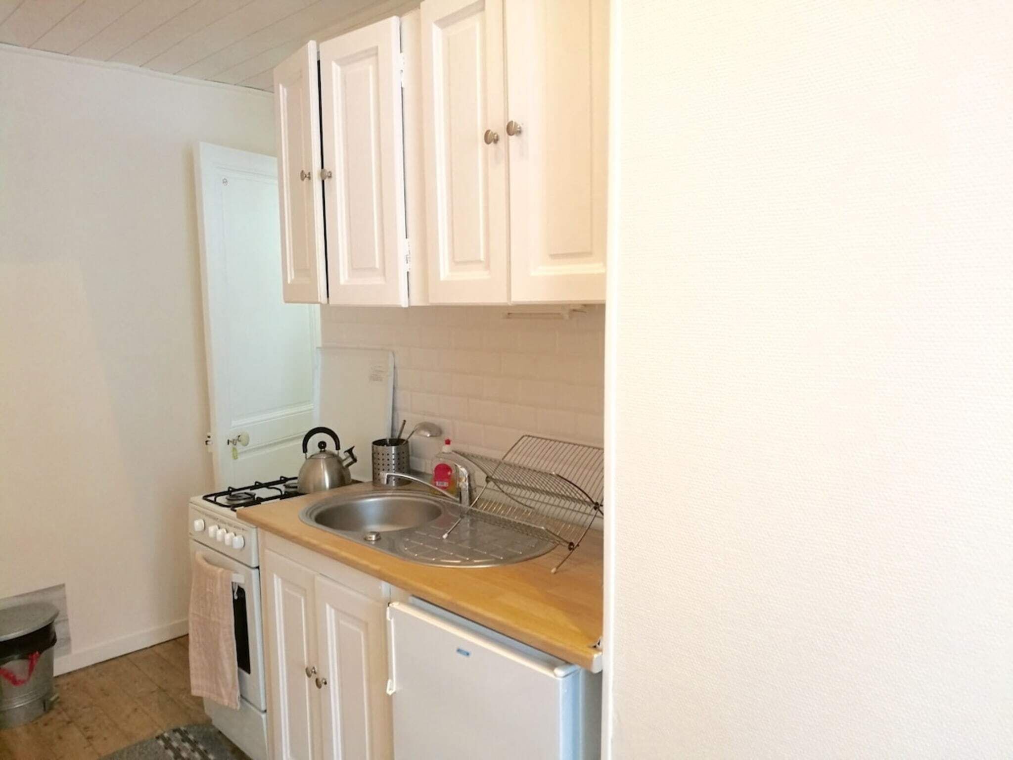 Une cuisine compacte avec des meubles blancs, une cuisinière à gaz, un évier et un petit réfrigérateur.