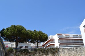 A multi-story building with balconies, a stone wall, and a large tree in front.