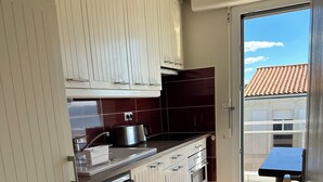 Een keuken met witte kastjes, een vaatwasser en een kookplaat. Er is een raam met uitzicht op een gebouw met een pannendak.