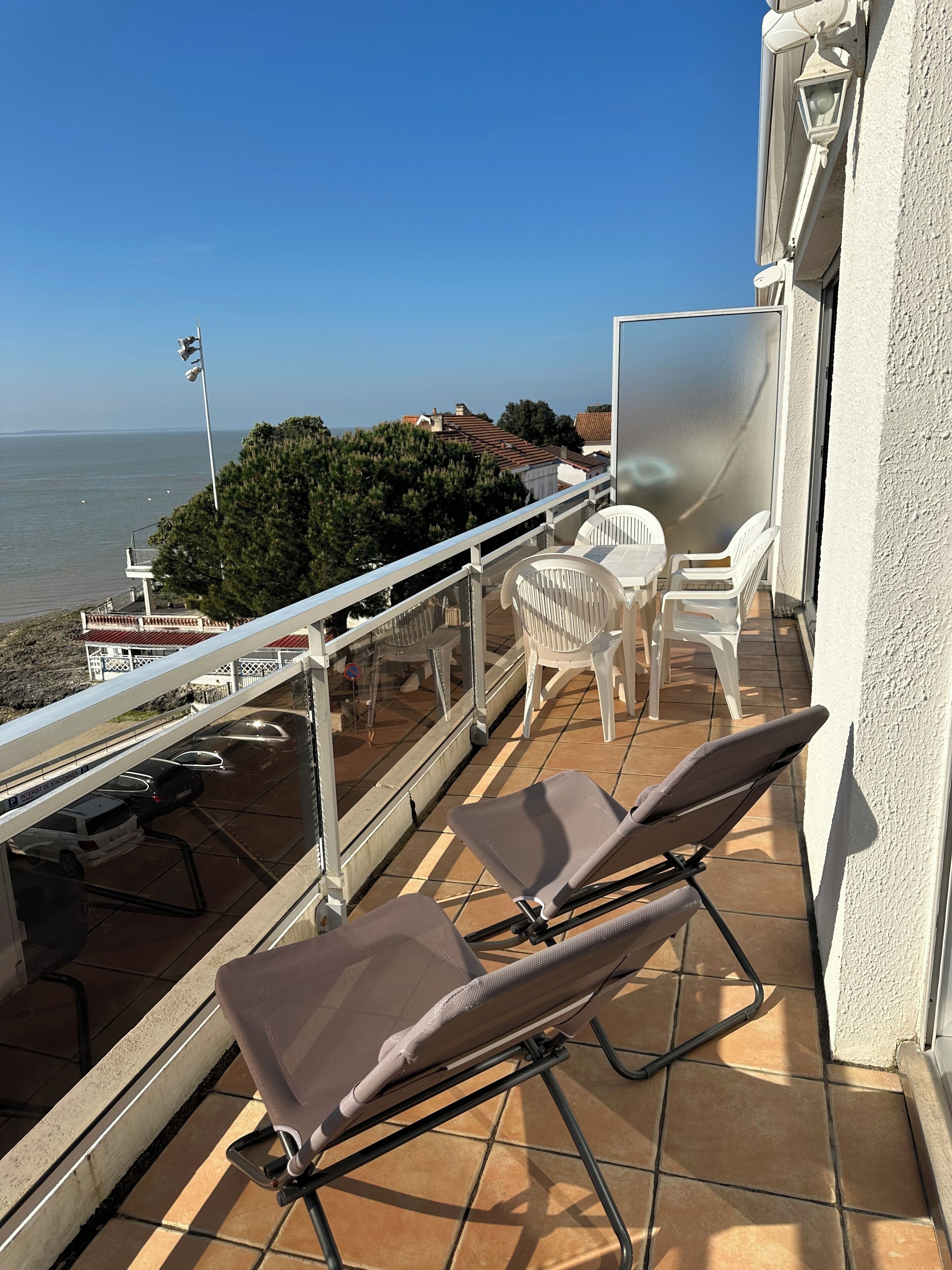 Un balcon avec deux chaises longues, une porte vitrée et une vue sur la mer.