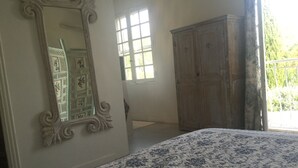 A bedroom with a bed, a large mirror, a wardrobe, and a window with a view of greenery. - Magnificent in the heart of Provence (Maillane)