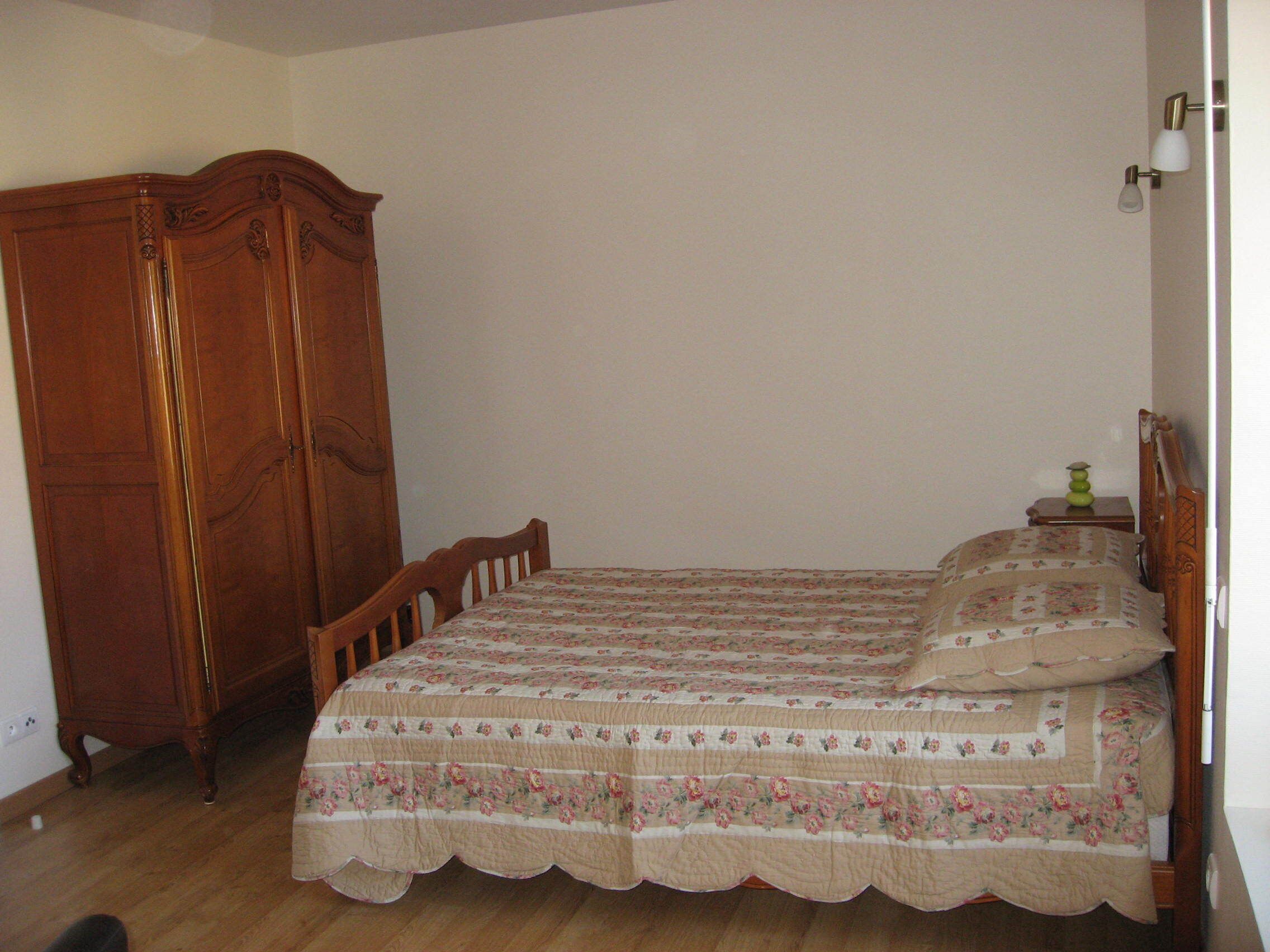 A bedroom with a wooden wardrobe, a bed with floral bedding, and a nightstand with a lamp.