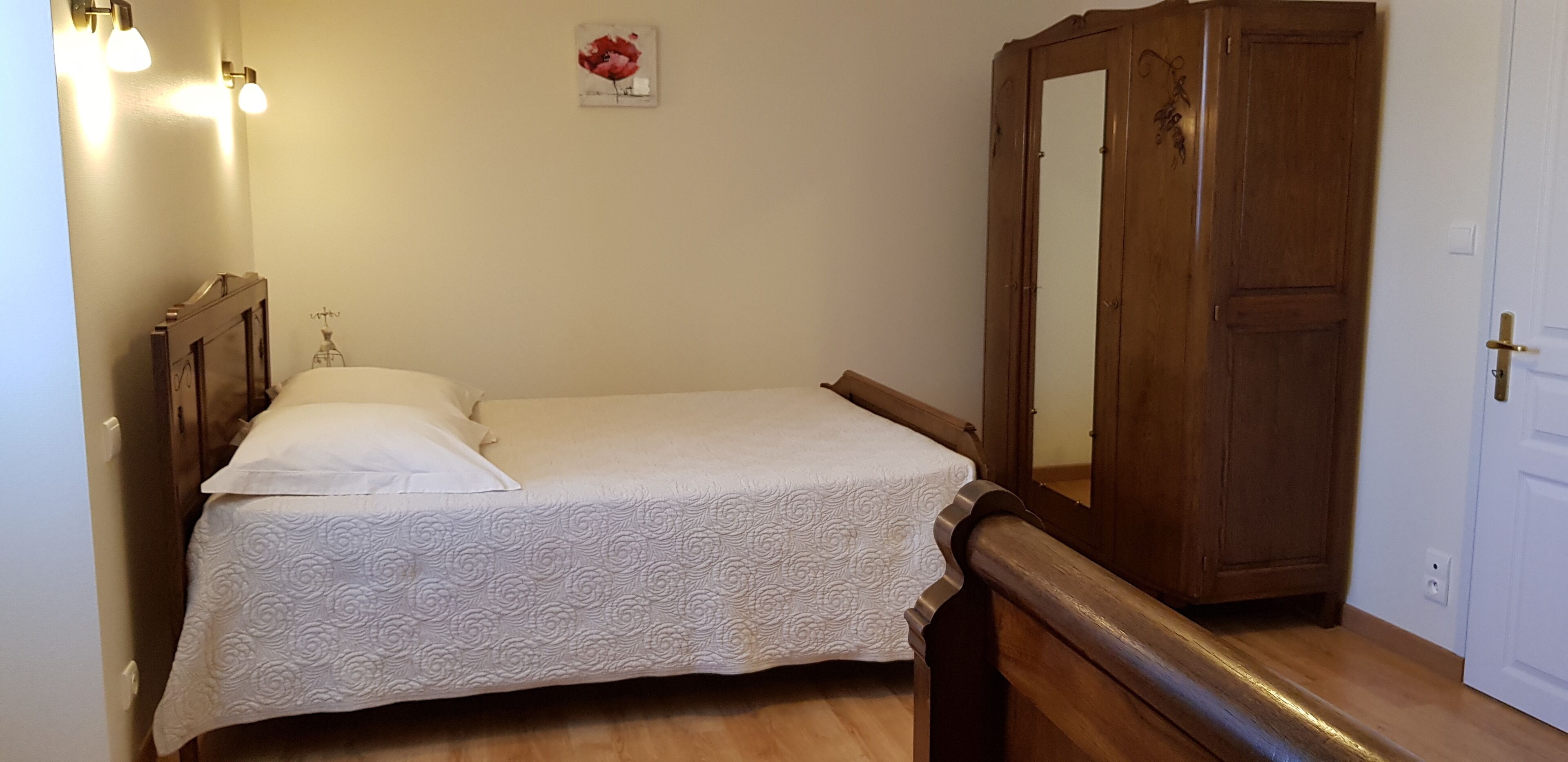 A bedroom with a bed, a wooden wardrobe, and a mirror.