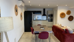 A modern kitchen with built-in appliances, a dining area with a table and chairs, and a red sofa. - New apartment, 4 people, ground floor, town center. (Cassis)
