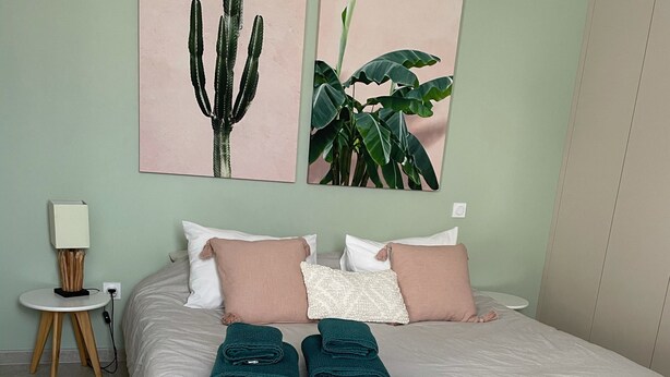 A bedroom with a bed, pillows, a bedside table, a lamp, and artwork on the wall. - New apartment, 4 people, ground floor, town center. (Cassis)