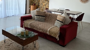 A modern living room with a red sofa, a glass coffee table, and a dining area with a white table and red chairs. - New apartment, 4 people, ground floor, town center. (Cassis)