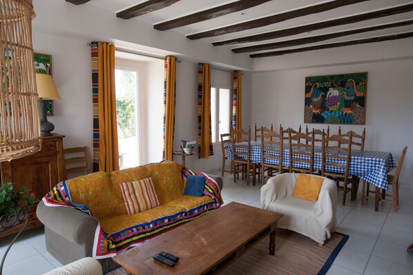 A living room with a sofa, a coffee table, a dining table with chairs, and a painting on the wall.
