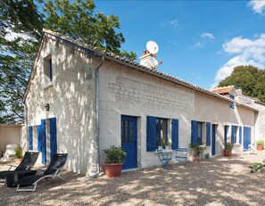 Un bâtiment blanc avec des volets bleus, une antenne parabolique et des places assises à l’extérieur.