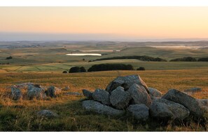 A rural landscape with rolling hills, a pond, and a stone wall in the foreground.