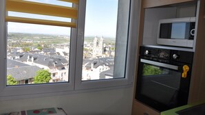 Eine Küche mit Blick auf eine Stadtlandschaft, darunter eine Kirche, durch ein Fenster mit gelben Jalousien.