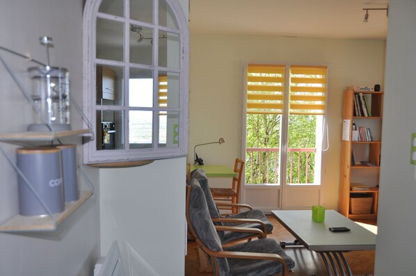 A room with a dining table, chairs, a window with blinds, a bookshelf, and a radiator.