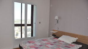 Ein Schlafzimmer mit einem Bett, einem Nachttisch, einer Lampe und Blick durch eine Schiebetür.