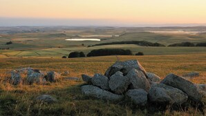 A rural landscape with rolling hills, a pond, and a stone wall in the foreground.