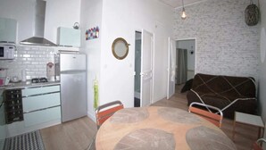 A compact kitchen with modern appliances, a dining area with a round table, and a living space with a sofa and a patterned rug. - Résidence Les Althéas - Apartment 3 (Villers-sur-Mer)