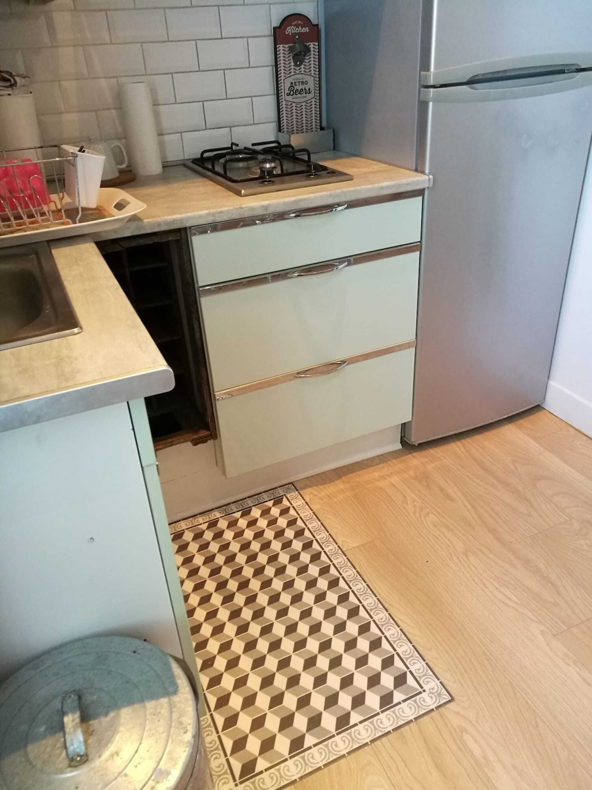 Eine Küche mit einem Gaskochfeld, einem Edelstahlkühlschrank und einem Teppich mit Muster.